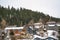 Mountain homes with snow covered roofs aginst coniferous trees and cloudy sky