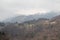 Mountain landscape. Bare trees on hills with snow peaks on background