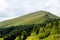 Mountain landscape with high green peak and blue sky with clouds.