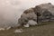 Mountain landscape - huge grey boulder with cracks, splits on slope, white fluffy dense cloud and dim green grass meadow