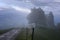 Mountain landscape shortly after spring rain. Slovenian Alps. Forest Road, venerable tree, fog, clouds and peaks. The village of J