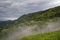 Mountain landscape shortly after spring rain. Slovenian Alps. Forest Road, venerable tree, fog, clouds and peaks. The village of J