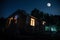 Mountain night landscape of building at forest at night with moon or vintage country house at night with clouds and stars. Summer