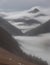 Mountain pass shrouded in mist in muted brown and gray hues, while creating mist with gentle white brush strokes.