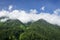 Mountain peaks covered with green forest against the blue summer sky with white clouds. Landscape of georgian nature