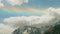 Mountain peaks covered with snow woth thick fluffy clouds and a rainbow above them. Nice view of russian nature.