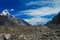 Mountain range snow peaks above glacier covered with gray stones