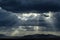 Mountain ranges under thick bank of rain clouds and rays of sunlight