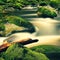 Mountain river with blurred waves of clear water. White curves in rapids between mossy boulders and bubbles create trails.