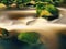 Mountain river with blurred waves of clear water. White curves in rapids between mossy boulders and bubbles create trails.