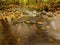 Mountain river with low level of water, gravel with first colorful leaves. Mossy rocks and boulders on river bank.