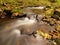 Mountain river with low level of water, gravel with first colorful leaves. Mossy rocks and boulders on river bank.