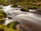 Mountain river in motion over big mossy boulders.