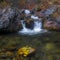Mountain river with small waterfall with clear water falling down wet boulders