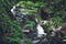 Mountain river waterfall among stones, green grass and ferns