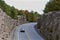 Mountain road cut through the pink granite. Landscape with rocks, autumn leaf color, and beautiful asphalt road in autumn. Transpo