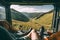 Mountain scenery view as seen from inside a campervan, with legs and a cup of coffee visible in the foreground. Ai generated