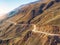 Mountain serpentine in the dawn sunlight. Dangerous narrow dirt mountain road through the hills to a high-altitude village. Aerial