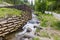 Mountain stream with artificial waterfalls and wooden logs crib wall