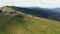 Mountain top, tourist destination. Car is driving on dirt road, people walk on a chairlift above slope of mountain