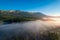 Mountain with visible silhouettes forest tree through morning colorful fog sunrise, aerial top view