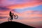 Mountainbiker doing wheelie in sunset sky on hill