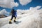 A mountaineer with a backpack walks in crampons walking along a dusty glacier with sidewalks in the hands between cracks