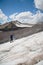 A mountaineer with a backpack walks in crampons walking along a dusty glacier with sidewalks in the hands between cracks