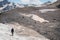 A mountaineer with a backpack walks in crampons walking along a dusty glacier with sidewalks in the hands between cracks