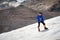 A mountaineer with a backpack walks in wheelchairs, stands on a dusty glacier with sneakers in the hands between cracks