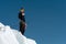 A mountaineer stands on the edge of a glacier with a snow shovel in his hands and shows Shak`s gesture against the blue