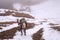 Mountaineer woman going down a mountain slope with skiing station in the mist on the distant background.