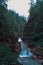 A mountainous clean blue river flows between stones rocks and mountains covered with green trees and bushes, rainy morning