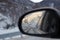 Mountains snowy landscape reflected in the car rear view mirror