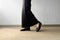 Mourning Feet Female in Black Flat Shoes and Black Dress Standing on the Concrete Background