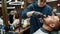 Moustache and beard grooming. Barber in black gloves cutting mustache of his client with electrical raser. Young man