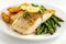 A mouth-watering plate of grilled cod fillet, garnished with a lemon slice, accompanied by roasted potatoes