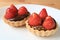 Mouthwatering a pair of chocolate tarts topped with fresh strawberries and edible gold powder served on white plate