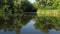 Movement along a quiet river with reflection of trees and sky in the water. Water lilies and reeds.