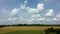 Movement of white clouds on blue sky over yellow ripened wheat field green trees