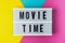 Movie time - text on a display lightbox on blue, yellow and pink background