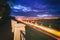 Moving car with blur light through city at night. Bridge over the river and the road. A view from the park from a height