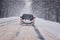 Moving car on snowy winter road among frozen forest after sleet. Cold weather, snowstorm, bad visibility, slippery road