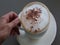 Moving coffee cappuccino froth latte drink cinnamon topping hand holding white mug on plate cinemagraph