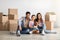 Moving day. Happy eastern family sitting among moving supplies paper boxes with belongings in empty apartment.