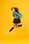 Moving with haste. Energetic child in midair yellow background. School girl in energetic jump. Back to school fashion
