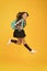 Moving with haste. Energetic child in midair yellow background. School girl in energetic jump. Back to school fashion