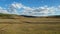 Moving rural scenery as seen through the vehicle window on the road, alongside a vast steppe meadow with hills on the horizon. Bea