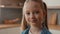 Moving shot close up little schoolgirl Caucasian child girl smiling looking at camera portrait at home kitchen cute 10s