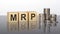 MRP - text on wooden cubes on a cold grey light background with stacks coins